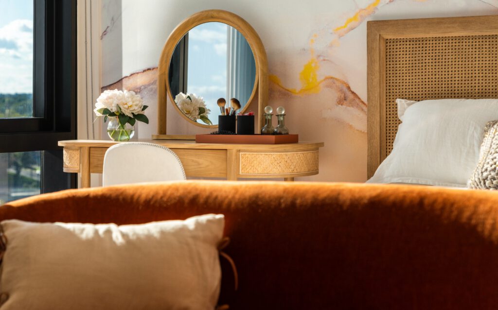 The bedroom of a luxury apartment at sunrise with plush linens on the bed and a makeup table next to a window with city views