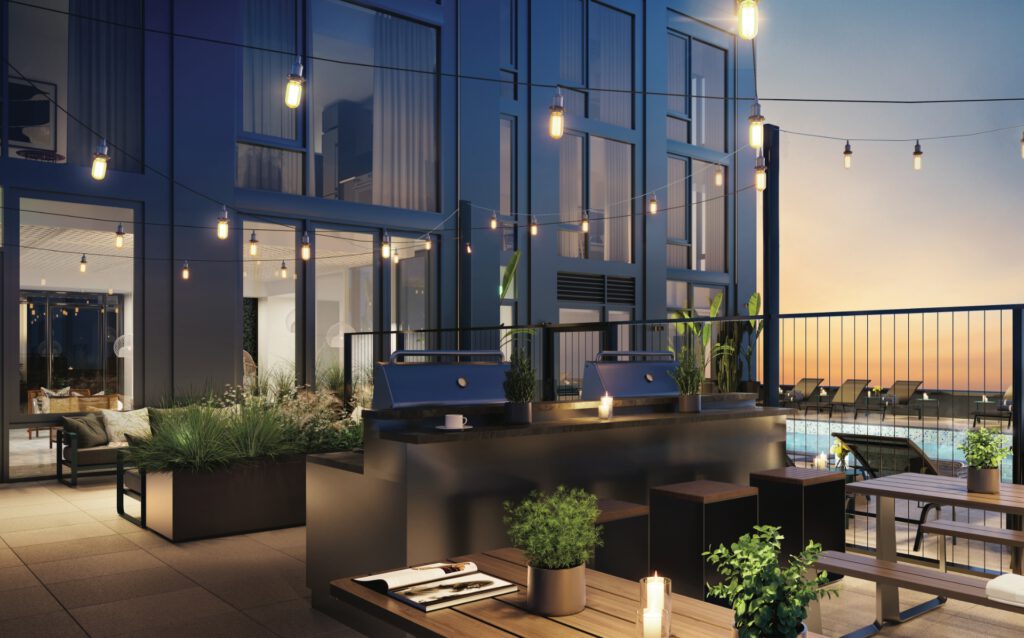 String lights hung over BBQ grills and planters on the luxury amenity terrace of a high rise apartment building at dusk