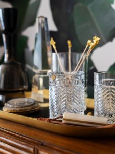 Glassware for a bar set up on an antique table with green, botanical wallpaper in the background