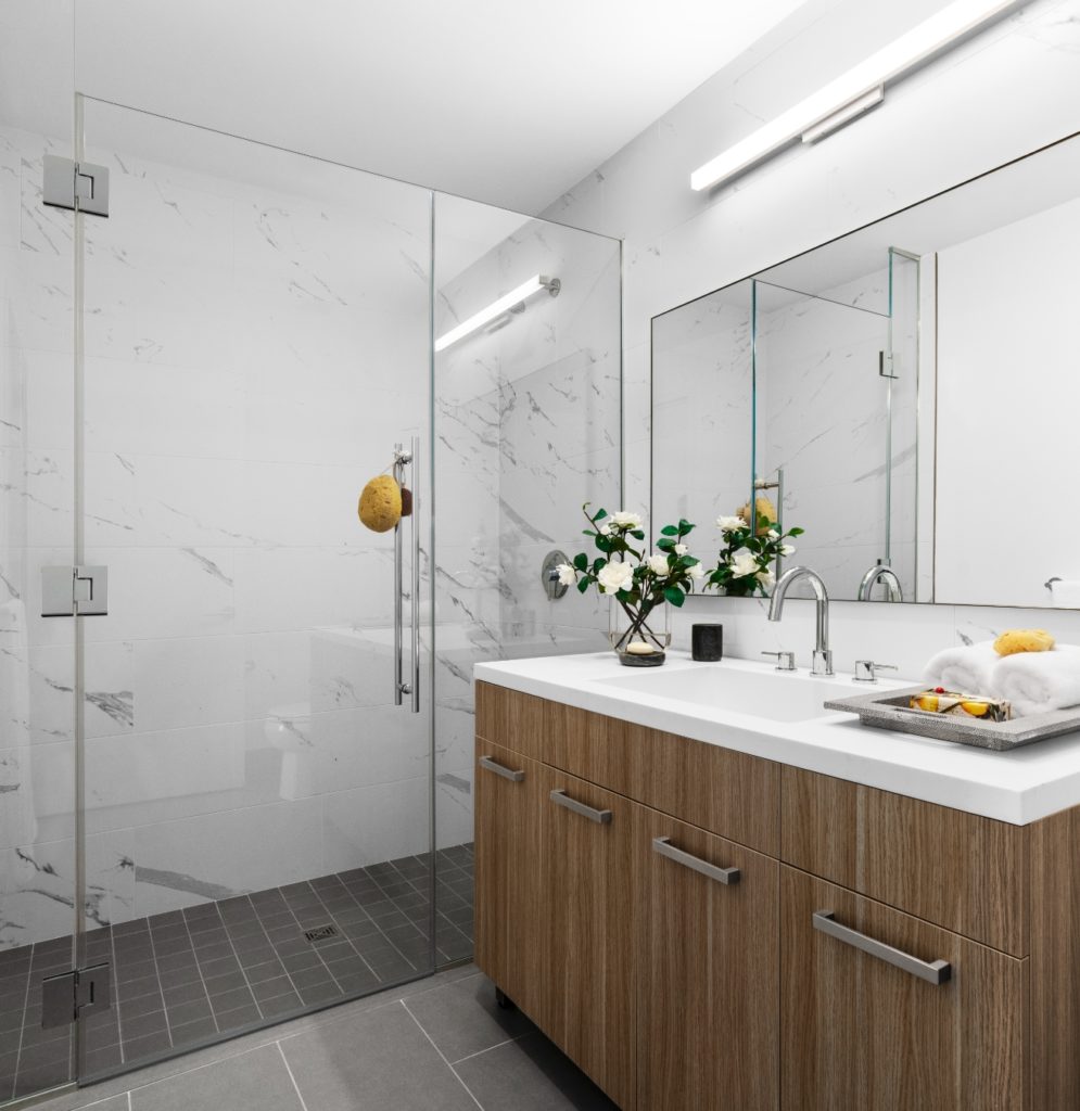 A modern luxury bathroom with a full height, glass walled shower and marble topped vanity with sink and mirror