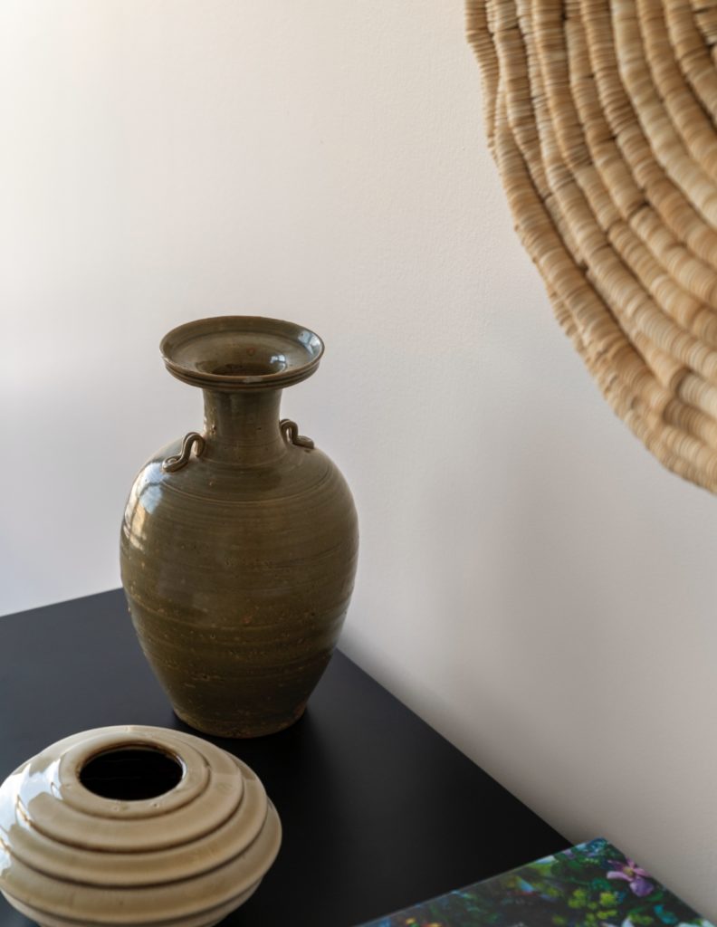 Elegant, modern ceramics in neutral colors positioned on a black pedestal with modern art hanging on the wall