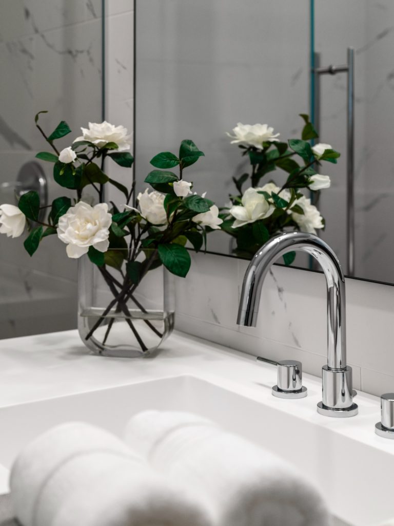 A marble bathroom countertop with hotel-style towels and a fresh flowers in a vase next to the sink and mirror