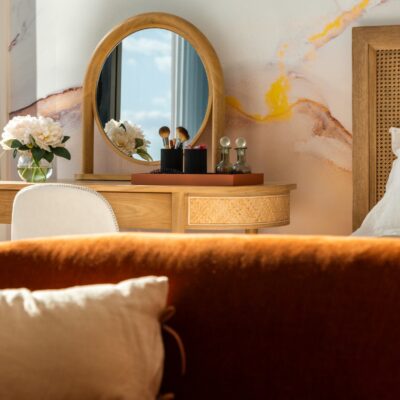 The bedroom of a luxury apartment at sunrise with plush linens on the bed and a makeup table next to a window