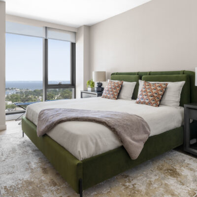 A king sized bed in a luxury apartment bedroom with floor to ceiling windows featuring views of The Long Island Sound