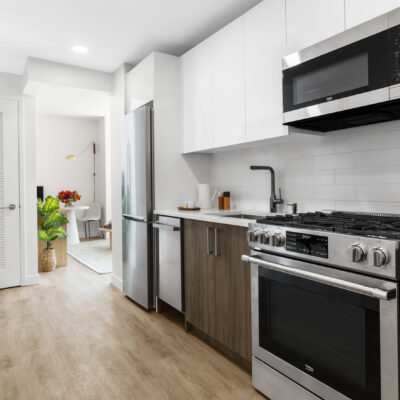 A galley style kitchen with white marble counters, stainless steel appliances, and a table, while a door opens to a bathroom