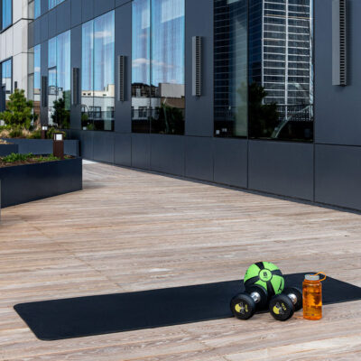 A yoga mat spread out on a rooftop amenity deck, with a water bottle, free weights, and exercise ball illuminated by the sun