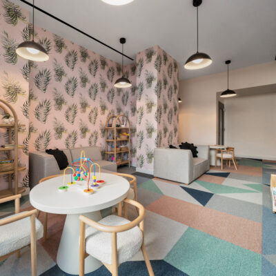 A children's play room with colorful carpet and floral wallpaper, couches, tables, and shelves with toys