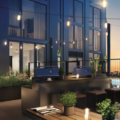 An outdoor dining area with picnic tables next to BBQ grills on the rooftop amenity deck of a high rise apartment building